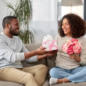 Image of a man playfully covering a woman's eyes while presenting her with a gift, depicting a sweet and romantic Valentine's Day surprise, ideal for showcasing thoughtful gift-giving.