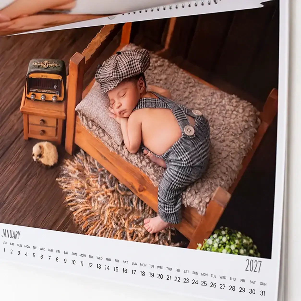 A 2022 calendar page featuring a photograph of a sleeping baby dressed in a vintage-style outfit with a matching cap, lying on a small wooden bed with a fluffy blanket. The scene includes a miniature nightstand with a toy bus and a small stuffed animal, set on a wooden floor. Ideal for baby shower gift ideas and personalised gifts in South Africa.