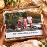 "Personalised photo book titled 'My Baby Journal' featuring a cover image of a pregnant woman in a yellow dress standing in a lush green outdoor setting. The photo book is placed on a wooden surface with a fringed yellow and grey blanket and some greenery in the background. Ideal for baby shower gift ideas and personalised gifts in South Africa."