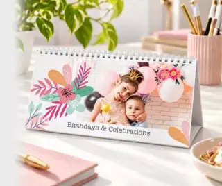 A 2024 wall calendar open to February, featuring a photo of a child holding a puppy in a field. The calendar is displayed on a white surface with decorative candles and vases nearby.