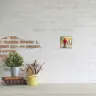 Small personalised canvas print featuring a child in a red coat, displayed on a white brick wall above a desk. The desk holds a potted plant, a stack of books, a yellow mug, and a jar of paintbrushes. Ideal for gifts for men, Christmas gift ideas, and personalised gifts in South Africa.