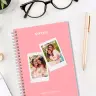 A personalised spiral-bound notebook with a pink cover featuring two polaroid-style photos of smiling women. The word "NOTES" is printed at the top in white. The notebook is placed on a white desk alongside a pair of black glasses, a gold pen, and a small plant. Ideal for gifts for her or Christmas gift ideas.