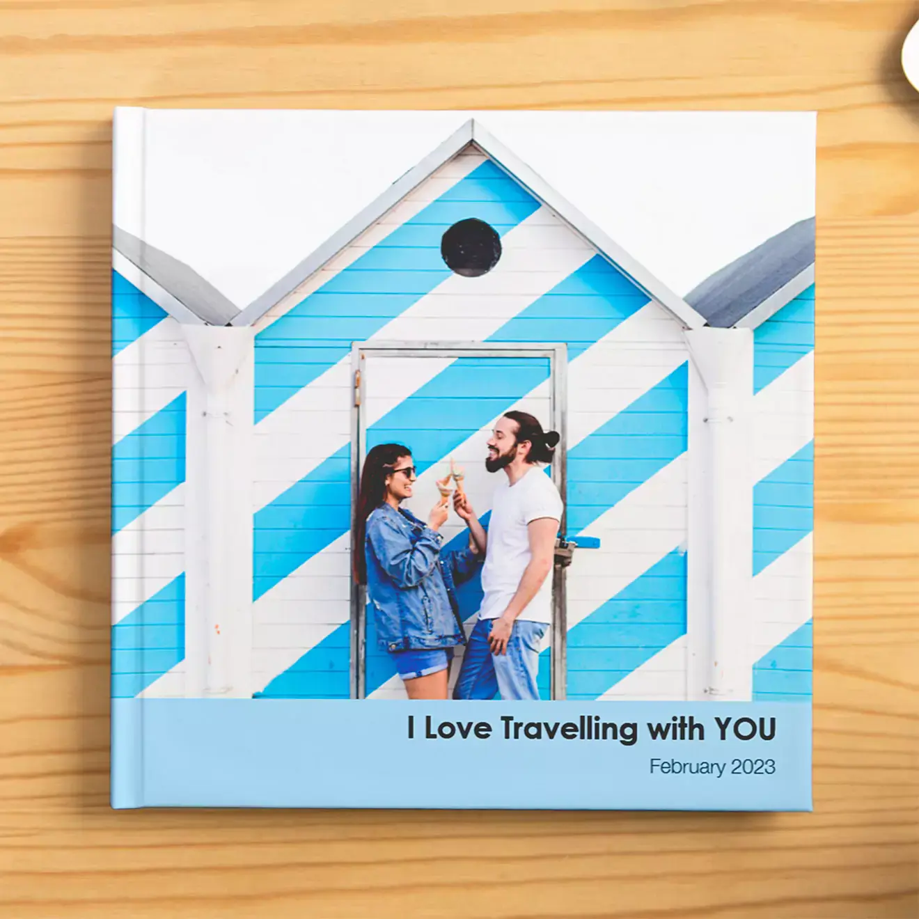 "Square photo book with a cover image of a couple standing in front of a blue and white striped beach hut, titled 'I Love Travelling with YOU' with the date February 2023. Ideal for personalised gifts in South Africa, photo albums, and travel memories."