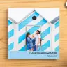 "Square photo book with a cover image of a couple standing in front of a blue and white striped beach hut, titled 'I Love Travelling with YOU' with the date February 2023. Ideal for personalised gifts in South Africa, photo albums, and travel memories."