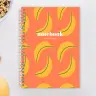 Spiral-bound notebook with a vibrant orange cover featuring a playful banana pattern. The word ''notebook'' is printed in white, with space for personalised text below. Ideal for recipe collections, journaling, or note-taking. Perfect as a gift for various occasions.