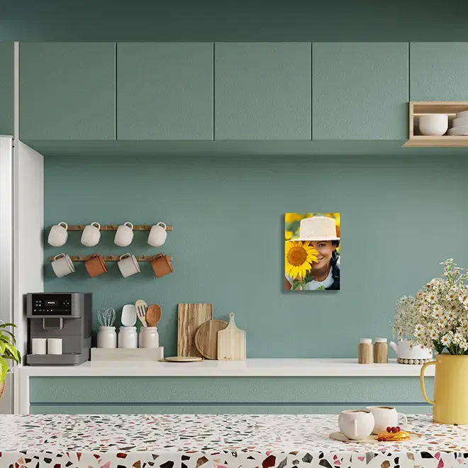 A modern kitchen with teal cabinets and a terrazzo countertop, featuring a personalised photo canvas on the wall. The canvas displays a person wearing a hat and holding a sunflower. The kitchen also includes a coffee machine, mugs, wooden utensils, and decorative plants. Ideal for personalised gifts in South Africa.