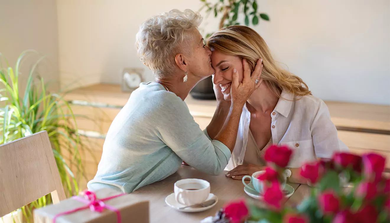 Daughter being kissed by her mother after receiving a personalised Mother's Day gift, capturing a tender and loving moment - banner