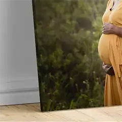 A budget-friendly canvas print featuring a photograph of a pregnant woman in a yellow dress, standing in a lush green outdoor setting. The canvas is propped against a white wall on a wooden floor, showcasing a high-quality, personalised gift option ideal for various occasions such as baby showers, Christmas, or Valentine's Day.