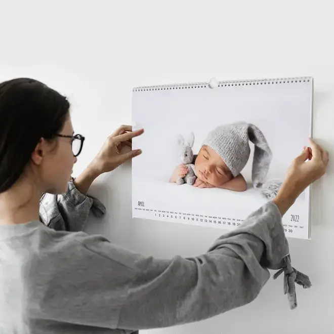 Photo of a lady hanging RapidStudio's personalised A3 wall calendar, featuring a charming picture of a cute baby, adding a personal and adorable touch to any room.