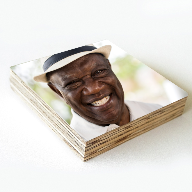 A stack of square photo prints featuring a smiling elderly man wearing a white hat. The photos are part of a funeral memories collection, capturing cherished moments and memories.