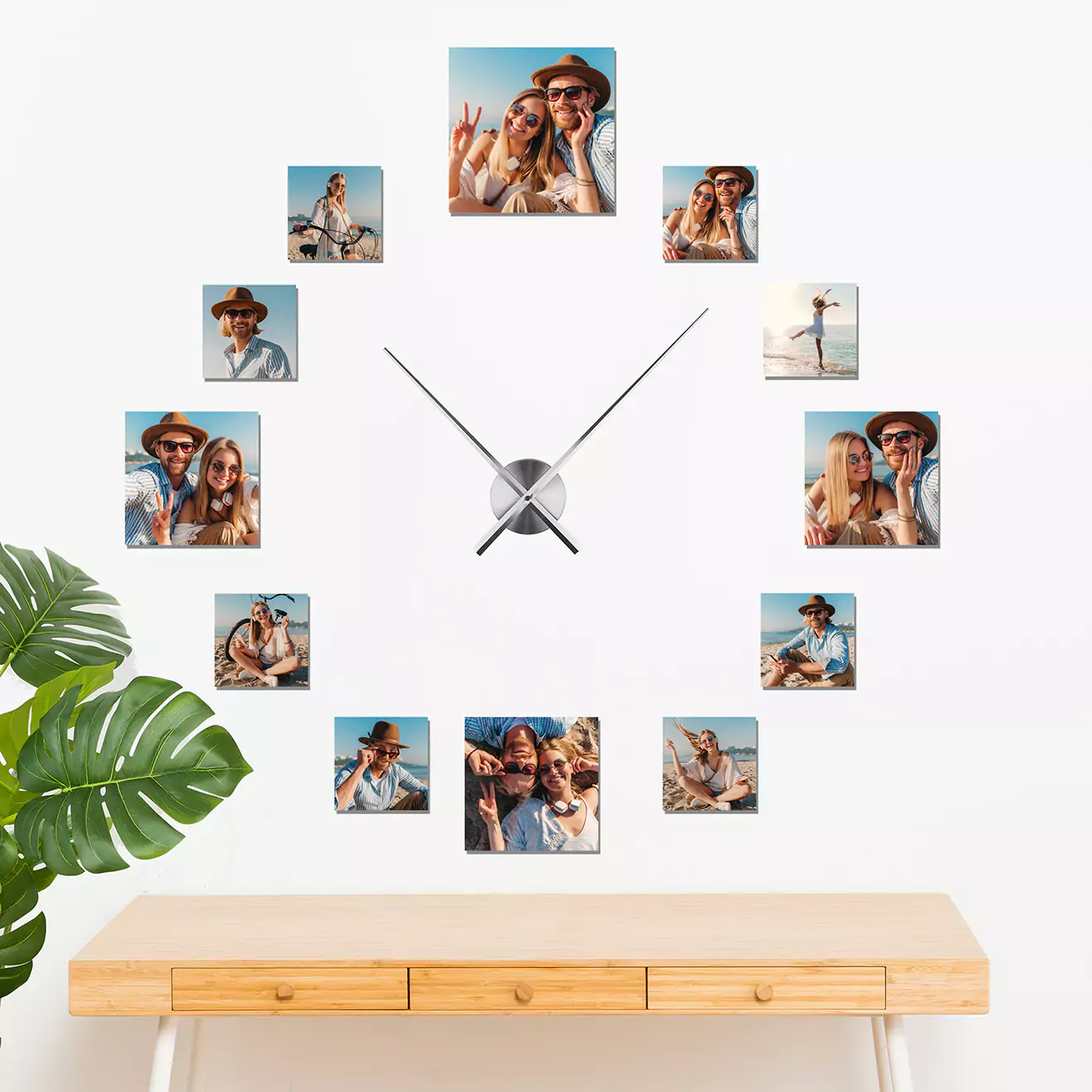 Wall clock with personalised photo frames arranged in a circular pattern, featuring various images of a couple in different poses. The clock is mounted above a wooden table with a green plant on the side.