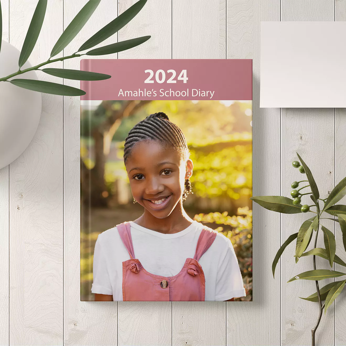 Personalised 2024 school diary featuring a young girl on the cover, set against a white wooden background with green foliage. Ideal for back-to-school gifts and personalised stationery in South Africa.