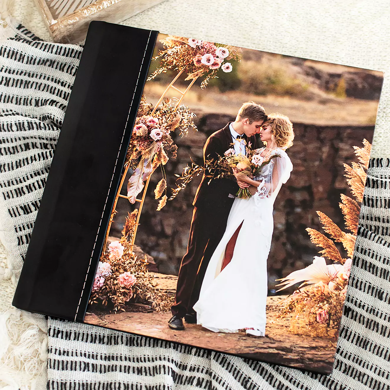 A beautifully crafted wedding photo album with a black spine, featuring a cover image of a newlywed couple sharing a kiss outdoors, surrounded by floral arrangements.