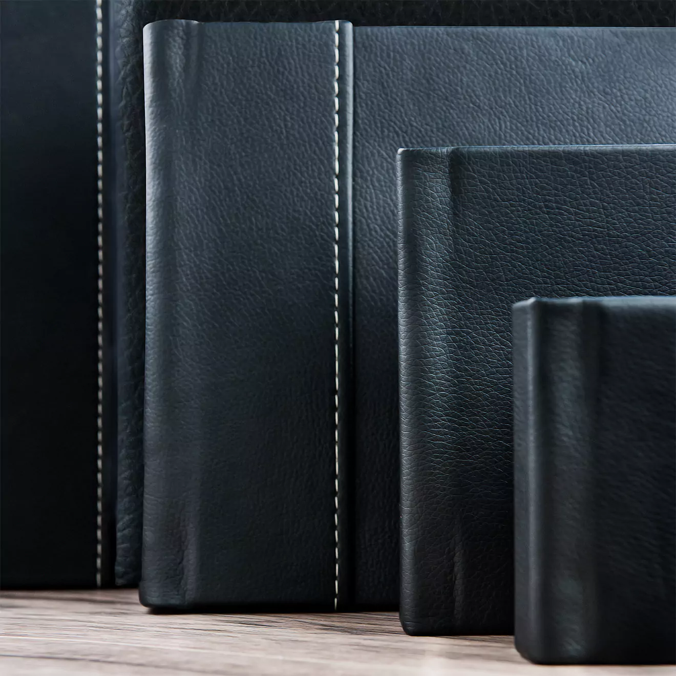 Collection of sleek, black leather photo albums with white stitching, displayed on a wooden surface. Ideal for sharing copies of wedding Albums, with the bride and grooms family.