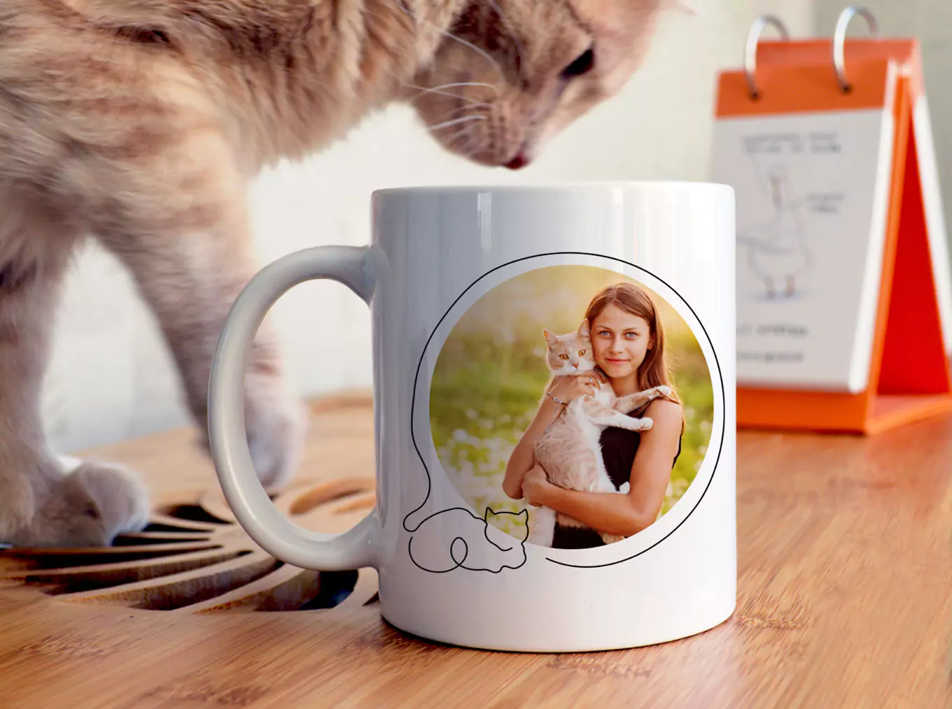 "Personalised white ceramic mug featuring a printed photo of a woman holding a cat, with a simple cat illustration below the image. Ideal for gifts for her, Christmas gifts, or personalised gifts in South Africa. Mug placed on a wooden surface with a cat and calendar in the background."