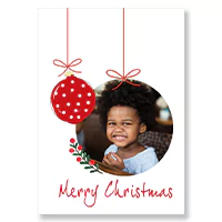 Christmas greeting card featuring a photo of a smiling child inside a circular frame. The card is decorated with a red bauble with white polka dots hanging from a ribbon. The text 'Merry Christmas' is written in red cursive at the bottom. Ideal for personalised Christmas gifts.