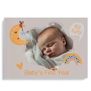 Hardcover baby photo album titled 'Baby's First Year' featuring a sleeping baby on the cover. The design includes cute illustrations of moons, stars, rainbows, and hearts in pastel colours. Ideal for baby shower gift ideas, personalised gifts in South Africa, and photo albums.