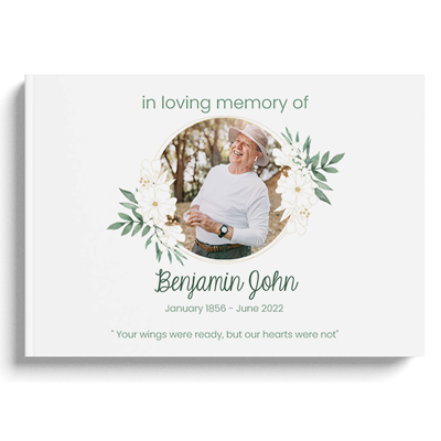 Hardcover photobook with a botanic theme, featuring a 'In loving memory of' design. The cover includes a circular photo frame surrounded by floral illustrations and greenery. Personalised with the name 'Benjamin John' and dates 'January 1856 - June 2022', along with a heartfelt quote. Ideal for memorial keepsakes and personalised gifts in South Africa.