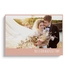 Hardcover photobook featuring a romantic wedding theme with a couple embracing and holding a bouquet of flowers on the cover. The book has a soft pink border and the text 'This is our beautiful story' at the bottom. Ideal for personalised gifts, photo albums, and special occasions.