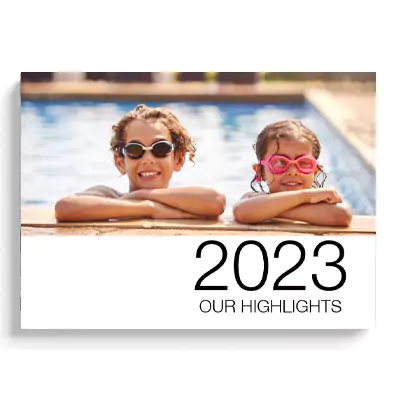 Hardcover photo book titled '2023 Our Highlights' featuring a cover image of two children wearing swimming goggles and leaning on the edge of a pool. Ideal for preserving memories, this photobook makes a perfect gift for various occasions such as Christmas, birthdays, and baby showers.