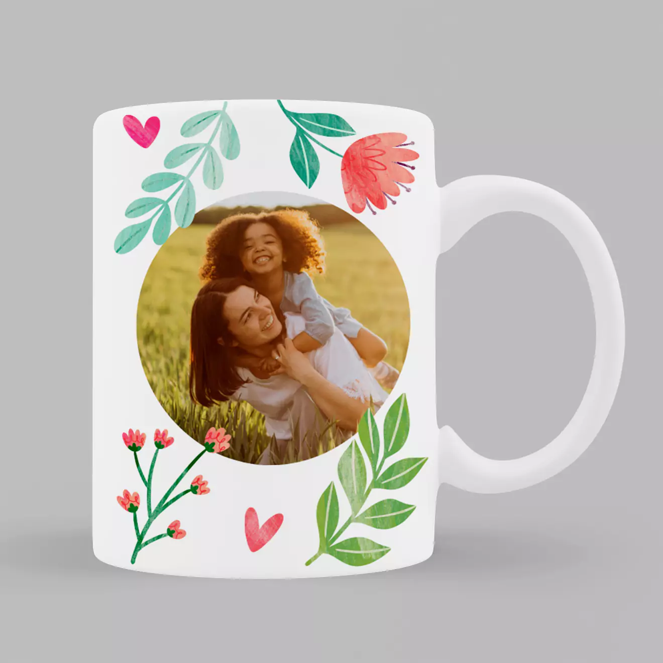 White ceramic mug featuring a floral theme with green leaves, pink flowers, and hearts. The centre displays a circular photo of a mother and child. Ideal for personalised gifts, especially for Mother's Day or birthdays. Suitable for gifts for her and Christmas gift ideas.