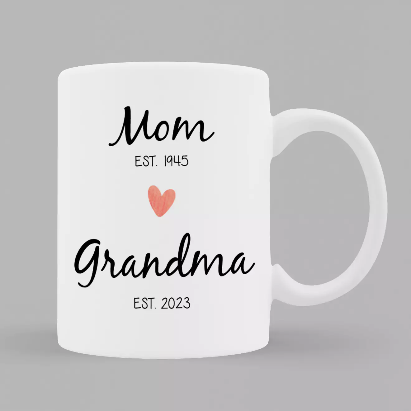 White ceramic mug featuring a generational theme with the words "Mom Est. 1945" and "Grandma Est. 2023" in black script. A small red heart is placed between the two texts. Ideal for personalised gifts in South Africa, perfect for Mother's Day or as a thoughtful gift for new grandmothers.