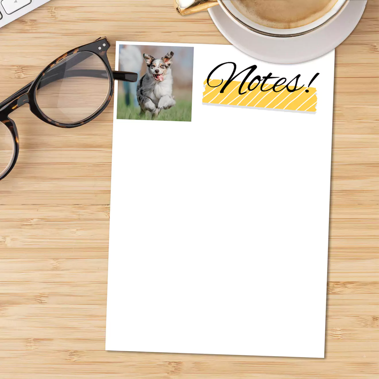 Theme notepad with 'Notes!' written at the top in elegant black script and a small photo of a dog in the upper left corner. The notepad is placed on a wooden surface next to a pair of glasses and a cup of coffee. Ideal for keeping organised and making lists.