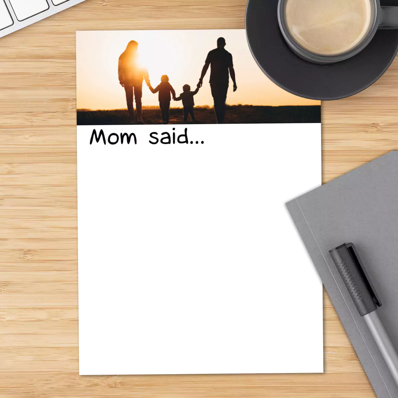 Theme notepad with 'Mom said...' text at the top, featuring a silhouette image of a family holding hands at sunset. The notepad has a blank white space for writing notes or messages. Ideal for personalised gifts, baby shower gift ideas, or Christmas gifts. Placed on a wooden desk with a coffee cup and a pen.