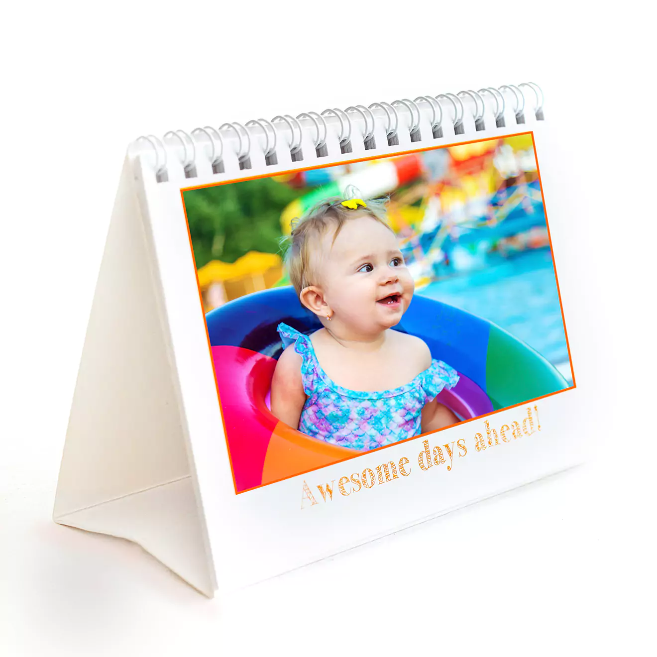 Personalised desk calendar featuring a spiral-bound design with a photo of a smiling baby in a colourful inflatable ring. The calendar has a white triangular stand and the text 'awesome days ahead!' printed below the photo. Ideal for gifts for her, baby shower gift ideas, and personalised gifts in South Africa.