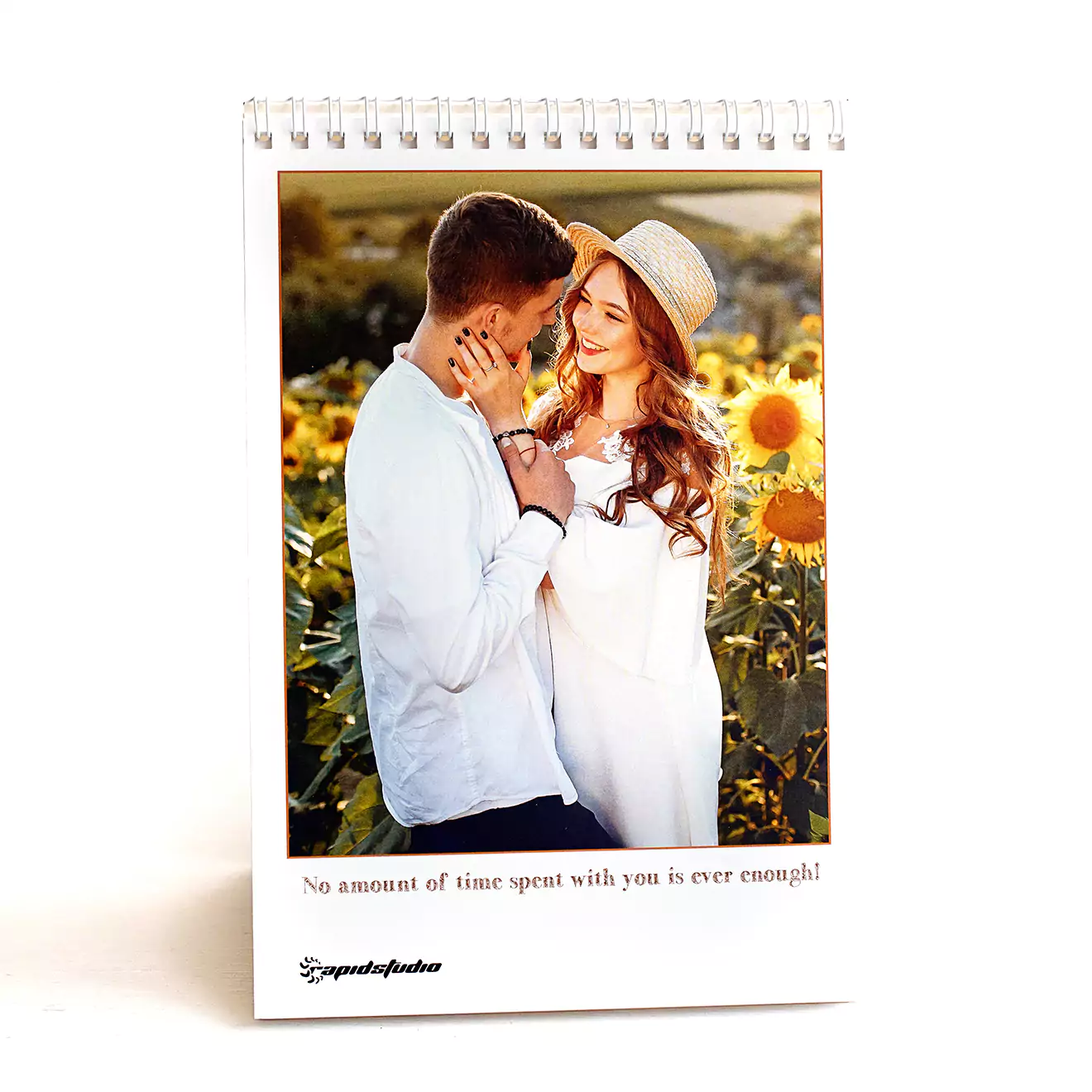 A personalised spiral-bound photo flipbook with a cover photo of a couple in a sunflower field and the text "Let's Make more Memories" at the bottom. The flipbook stands upright on a flat surface, making it ideal for displaying cherished memories. Perfect for gifts for men, Christmas gift ideas, or personalised gifts in South Africa.