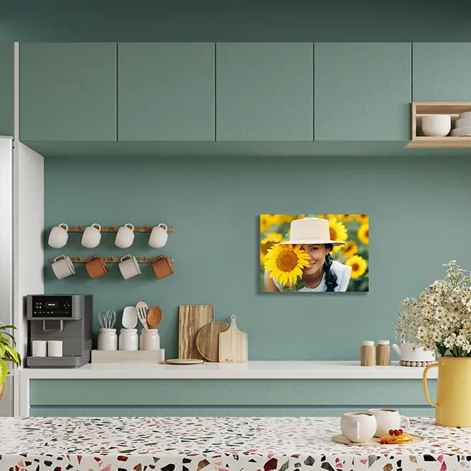 Modern kitchen with green cabinets and a terrazzo countertop, featuring a personalised photo canvas on the wall. The canvas displays a vibrant image of a person in a sunflower field. The kitchen decor includes a coffee machine, mugs, wooden cutting boards, and a vase with flowers. Ideal for personalised gifts in South Africa.