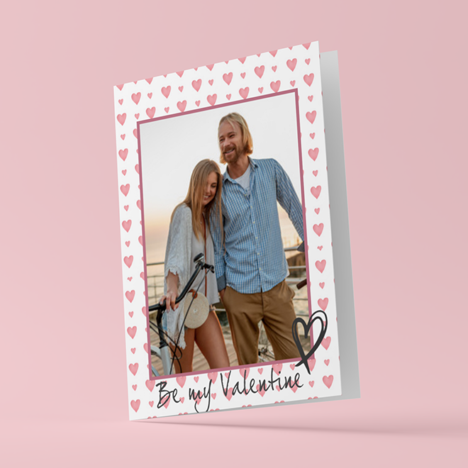 Valentine''s Day greeting card featuring a photo of a couple, with a white background adorned with pink hearts. The card has a message at the bottom that reads ''Be my Valentine'' in a handwritten style with a heart illustration. Ideal for personalised Valentine''s Day gift ideas.