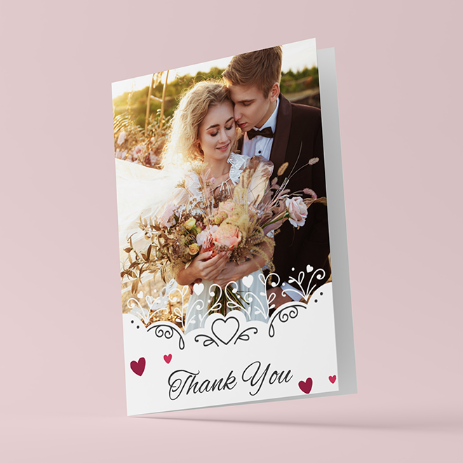 Elegant wedding thank you card featuring a romantic photo of a bride and groom holding a bouquet. The card has a white background with decorative floral and heart designs, and the words ''Thank You'' in stylish script at the bottom. Ideal for expressing gratitude to wedding guests.