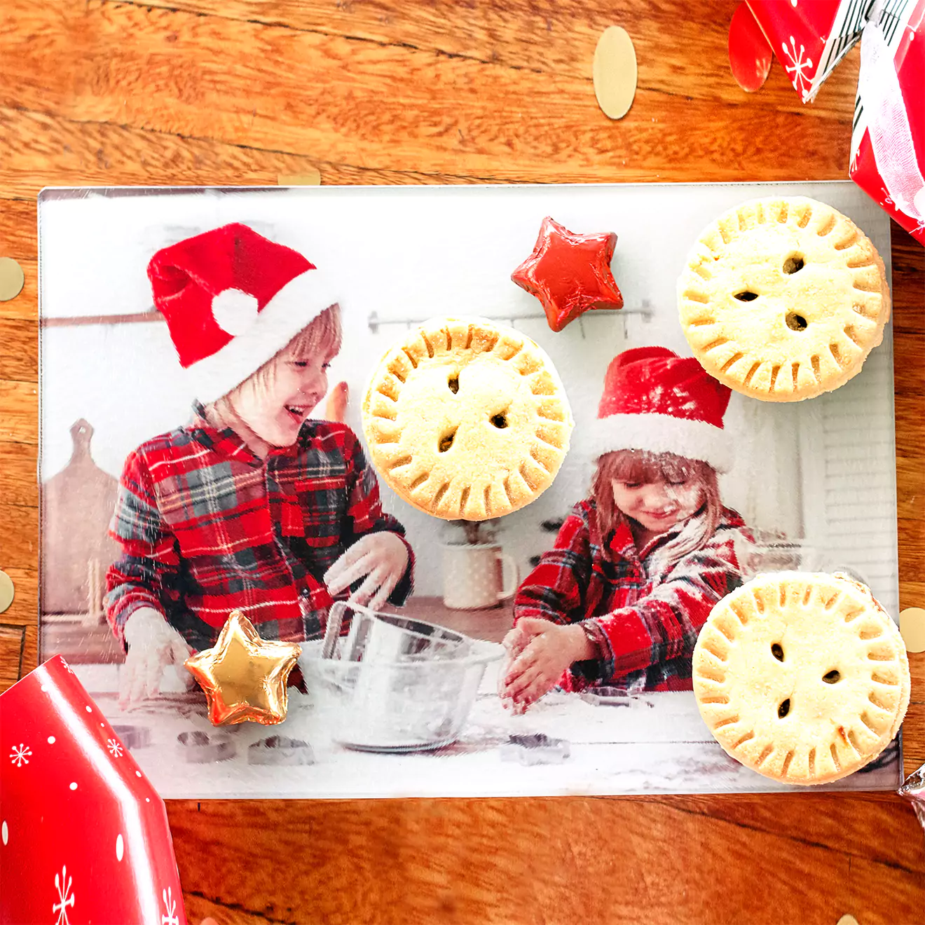 Festive photo of two children in Santa hats and plaid shirts on a personalised cutting board, baking in the kitchen, surrounded by mince pies and star-shaped cookies. Ideal for Christmas gifts, or to add a festive cheer to your kitchen