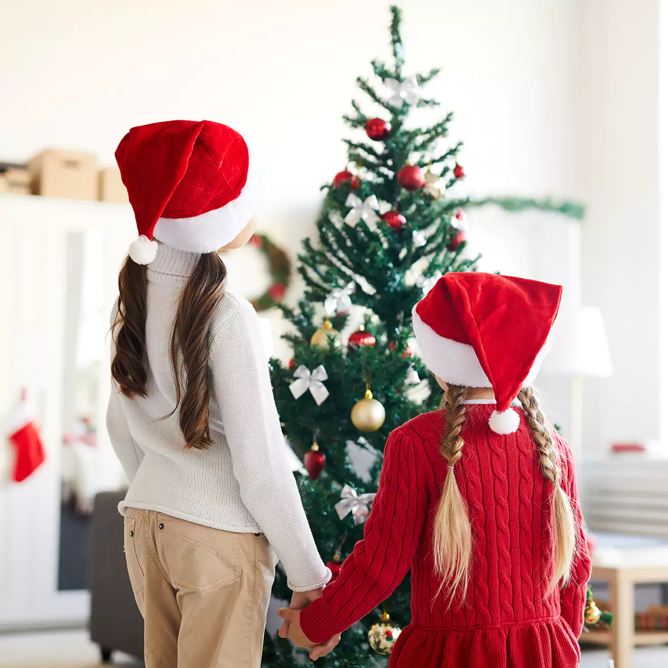 Image of children in Santa hats gazing admiringly at Christmas tree decorations, capturing their wonder and excitement at the sparkling lights and colourful ornaments of the festive season.