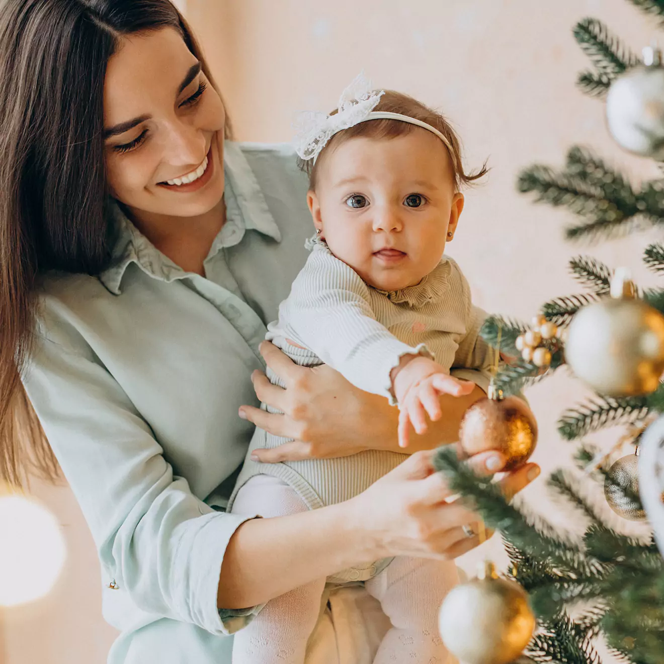 Image of a mother and her baby enjoying their first Christmas together, sharing a warm, festive moment beside a beautifully decorated tree, embodying the joy and special bond of the holiday season.