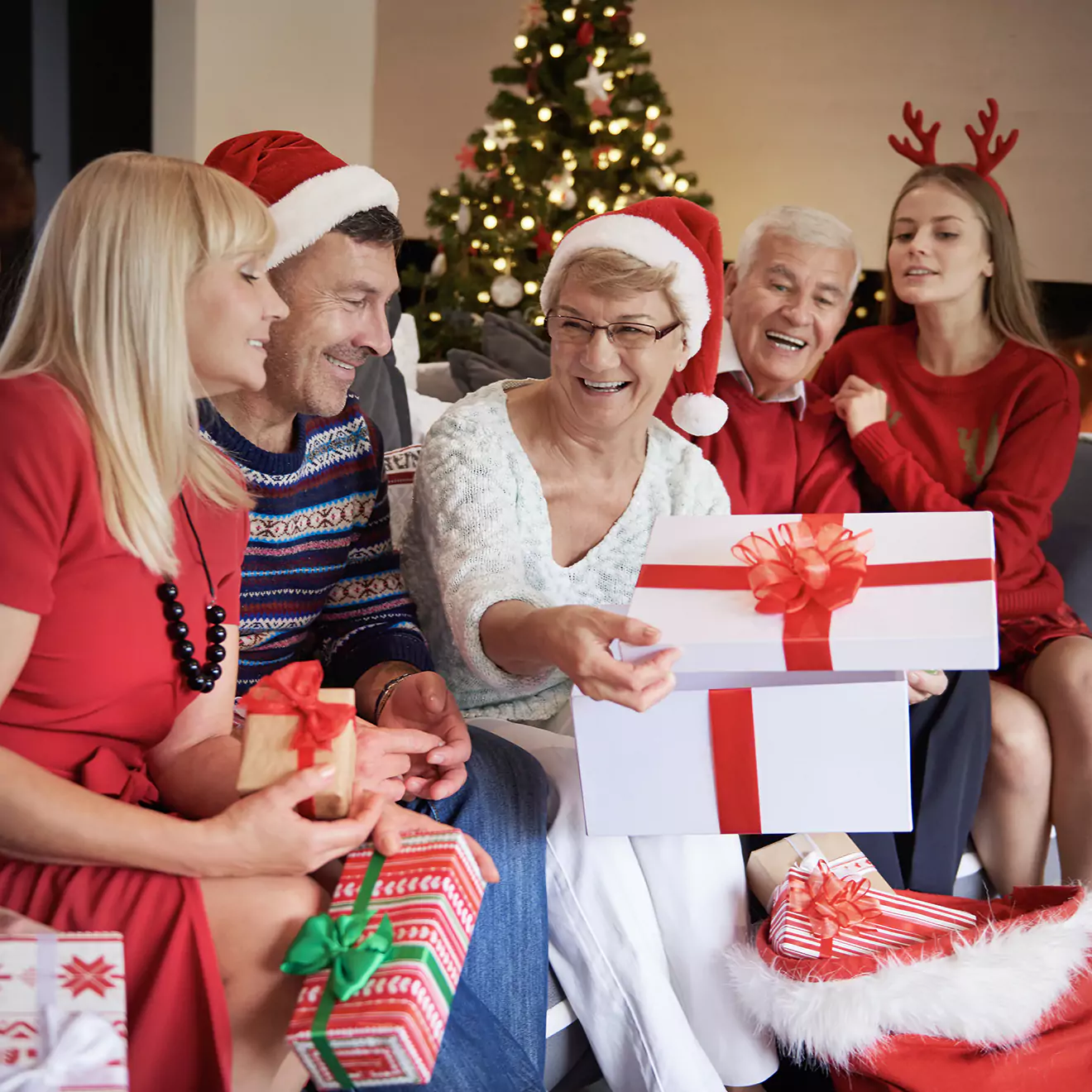 Image of a multigenerational family enjoying a gift exchange on Christmas, gathered around a tree in a warm, decorated living room, celebrating the holiday with joy and togetherness.