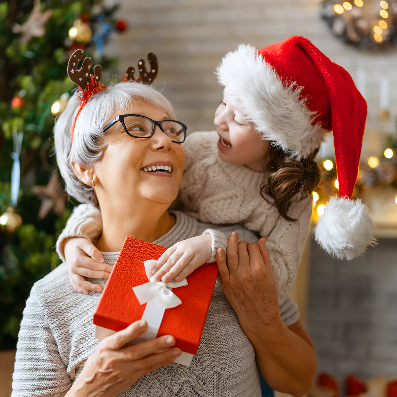 Image of a grandmother and granddaughter enjoying a Christmas gift exchange, sharing smiles and a warm embrace, capturing a heartfelt moment of generational bonding during the holiday festivities.