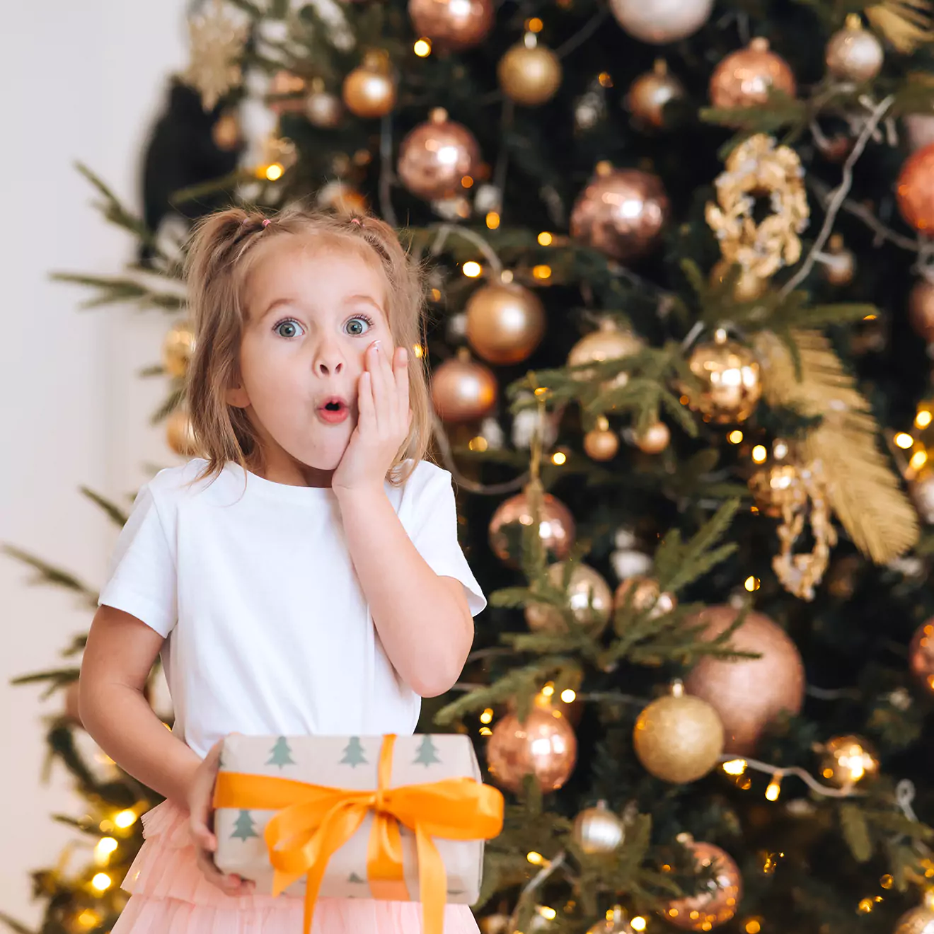 Image of a little girl expressing surprise and delight as she opens a Christmas gift, capturing the excitement and wonder of a child during the festive season.