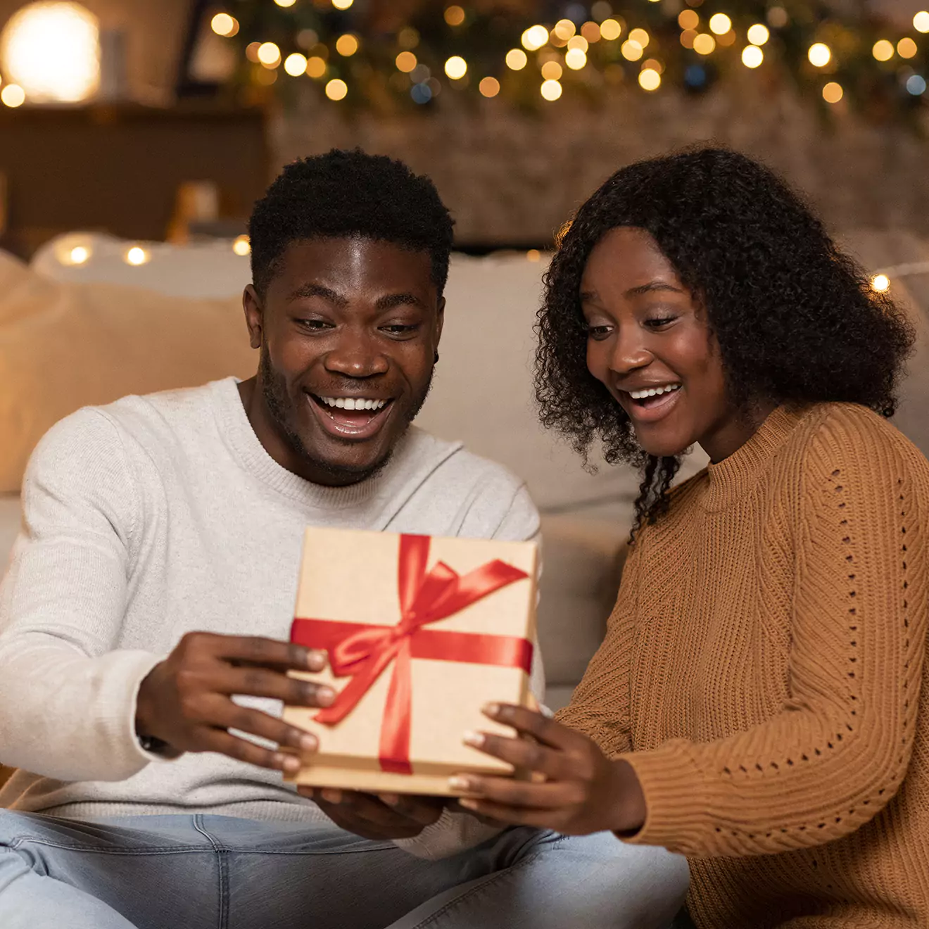 Image of a couple sharing a joyful moment while exchanging Christmas gifts, embracing and smiling in a cozy, festive setting, illustrating the love and happiness of the holiday season.