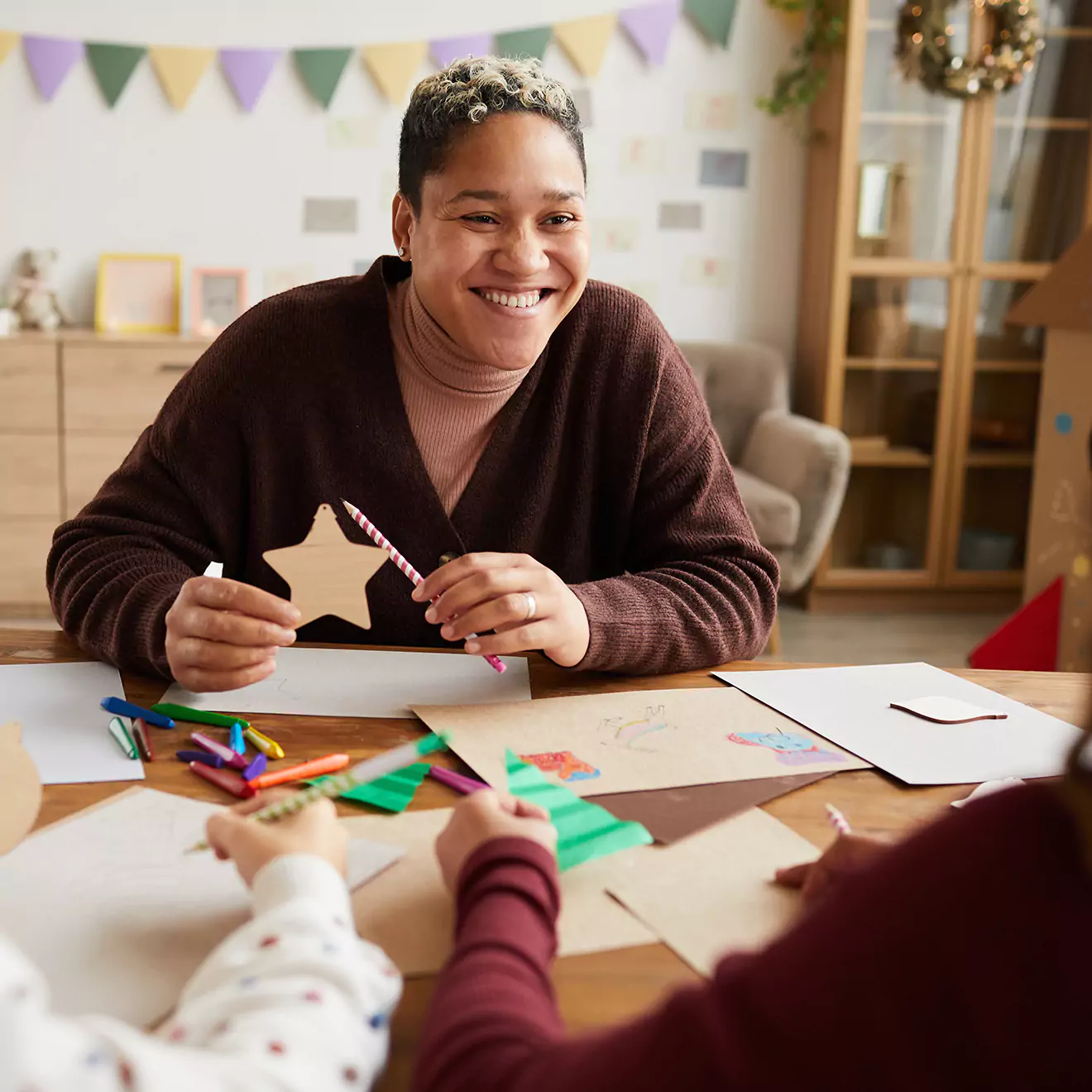 Image of a teacher and students crafting together for Christmas festivities, engaged in making holiday decorations in a classroom setting, fostering creativity and festive spirit among young learners.