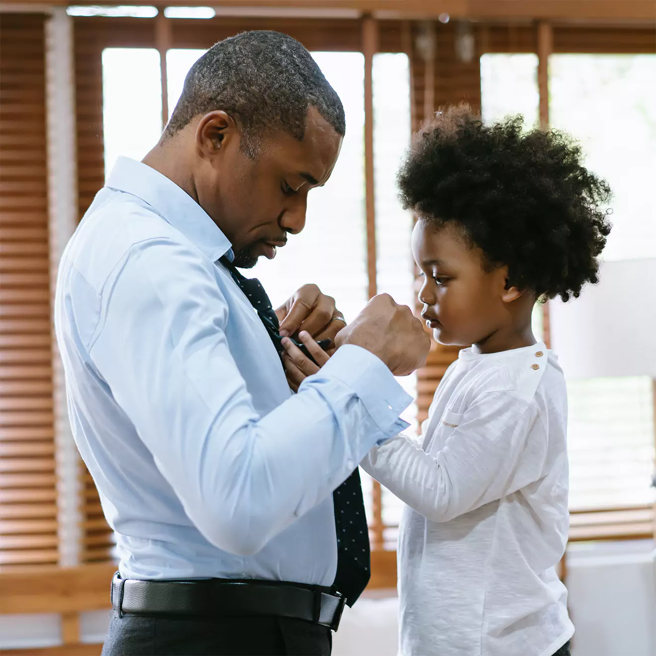 A youngster helping his dad with his tie, capturing a heartwarming moment. Perfect gifts for his office, such as personalised mugs or stationery, celebrating the bond between father and child. Thoughtful gift ideas in South Africa.