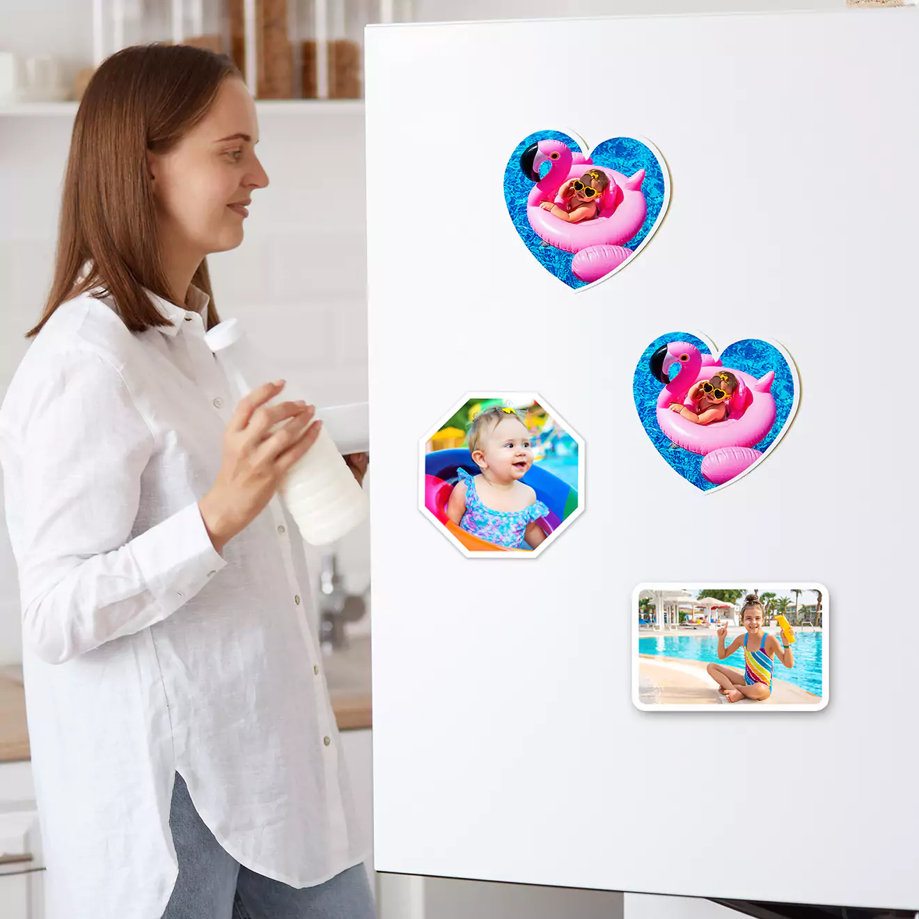 A woman in a white shirt stands in a kitchen holding a cup, looking at a white refrigerator adorned with four round photo magnets. The magnets feature colourful images of a child in various playful poses, making them ideal personalised gifts for occasions like Christmas or birthdays.