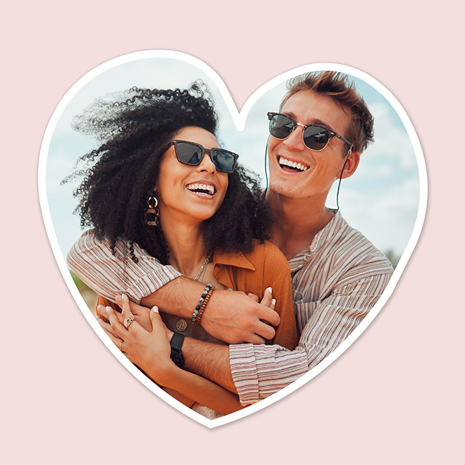 Heart-shaped photo featuring a smiling couple wearing sunglasses, with the woman in an orange top and the man in a striped shirt. The image is set against a light pink background, ideal for personalised gifts, photo albums, or Valentine's Day gift ideas.