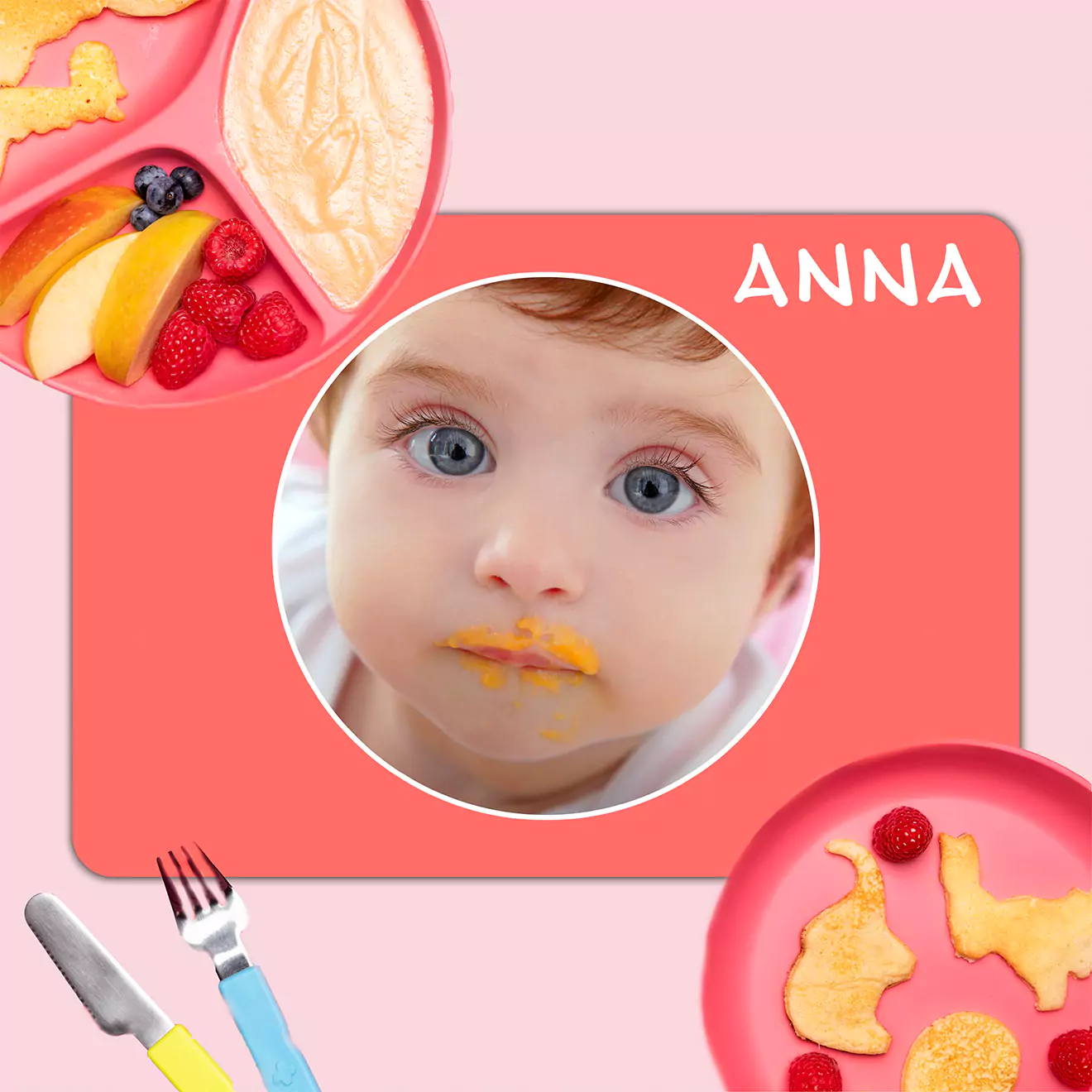 Personalised baby placemat featuring a photo of a baby with food on their face, set against a pink background. The placemat is adorned with the name "Anna" in white text. Surrounding the placemat are plates with fruit and utensils, making it a charming and practical gift for baby showers or young children.