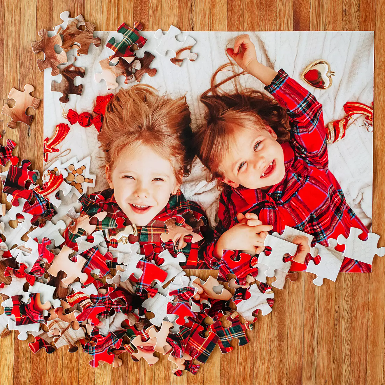 Personalised photo puzzle featuring two smiling children in red plaid shirts, lying on a white blanket. The puzzle pieces are scattered around the partially completed puzzle on a wooden surface. Ideal for gifts for men, baby shower gift ideas, Christmas gift ideas, and personalised gifts in South Africa.