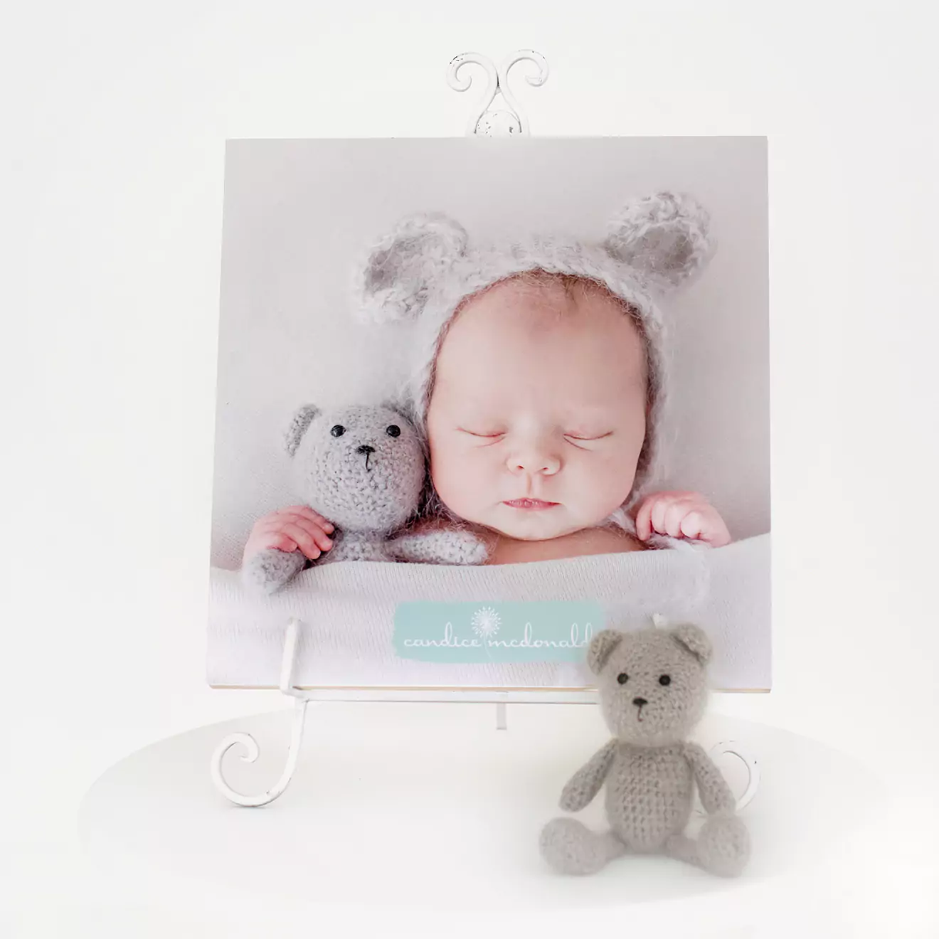 Square photo canvas featuring a sleeping baby wearing a grey knitted hat with bear ears, cuddling a small grey teddy bear. The canvas is displayed on a white decorative stand, with a matching grey teddy bear placed in front. Ideal for baby shower gift ideas or personalised gifts in South Africa.