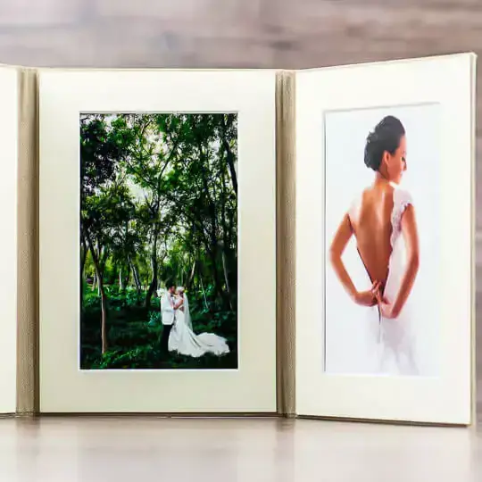 Elegant cream-coloured photo album with a tri-fold design, showcasing two wedding photographs. The left panel features a couple in a lush green forest, while the right panel displays a bride in a backless dress. Ideal for wedding memories, personalised gifts in South Africa, and photo albums.