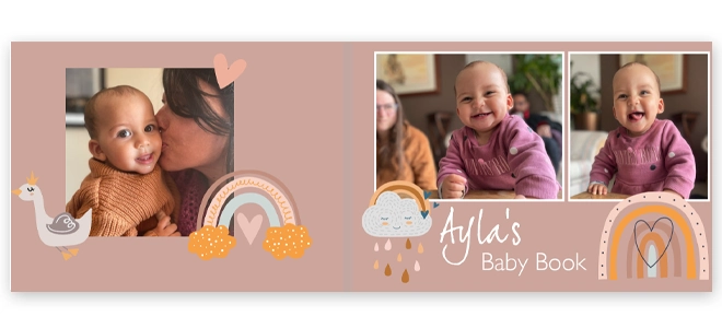 Personalised baby photo book cover titled ''Ayla''s Baby Book'' featuring a soft pink background with whimsical illustrations of rainbows, hearts, and a swan. The cover includes three photos of a smiling baby and a parent, making it a charming keepsake for baby shower or Christmas gift ideas.