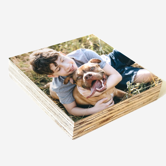 A square 20cm Shutter block with image of a young person hugging a happy dog while lying in the grass, designed for memorialising pets. shutter-block has a wooden texture on the sides.